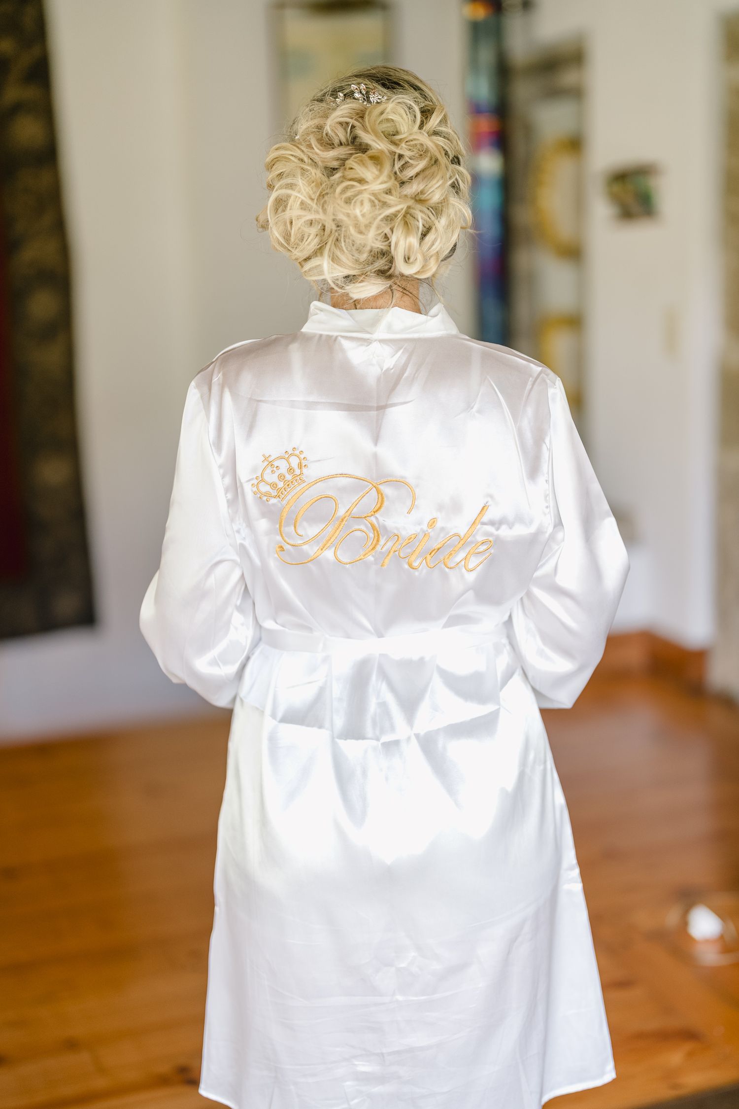 A white satin robe with 'Bride' embroidered in gold lettering displayed on a wooden table.