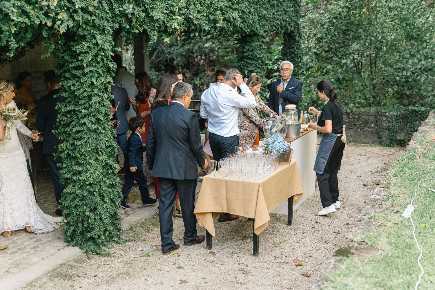 Os convidados do casamento reúnem-se em torno de mesas de buffet montadas ao ar livre, num exuberante jardim em ponte de lima