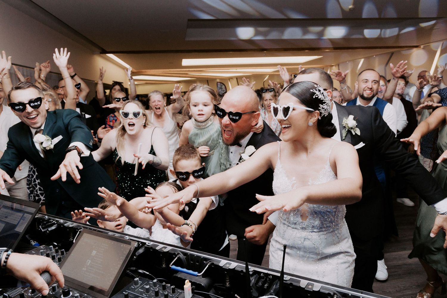 A large group of wedding guests dance enthusiastically together on a crowded dance floor during a celebration.