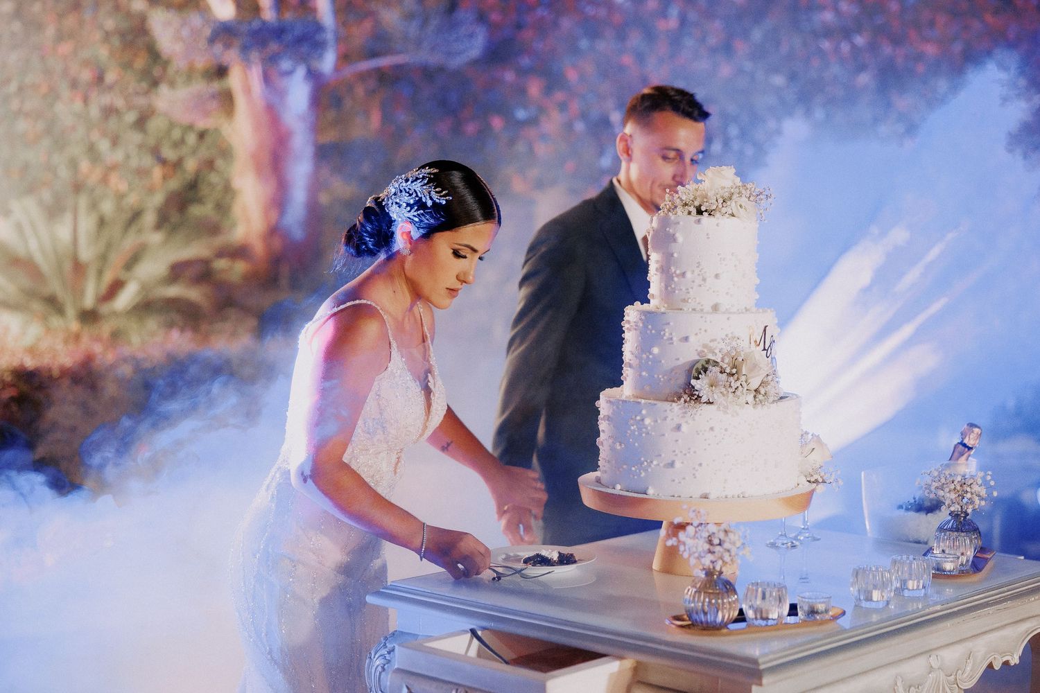 A couple cuts their elegant white wedding cake together on a misty table during their reception celebration.