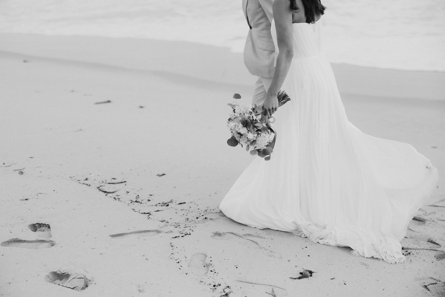 Fotografia em preto e branco mostrando a parte inferior de um vestido de noiva esvoaçante e patins em uma praia de areia. Set Lounge Azurara