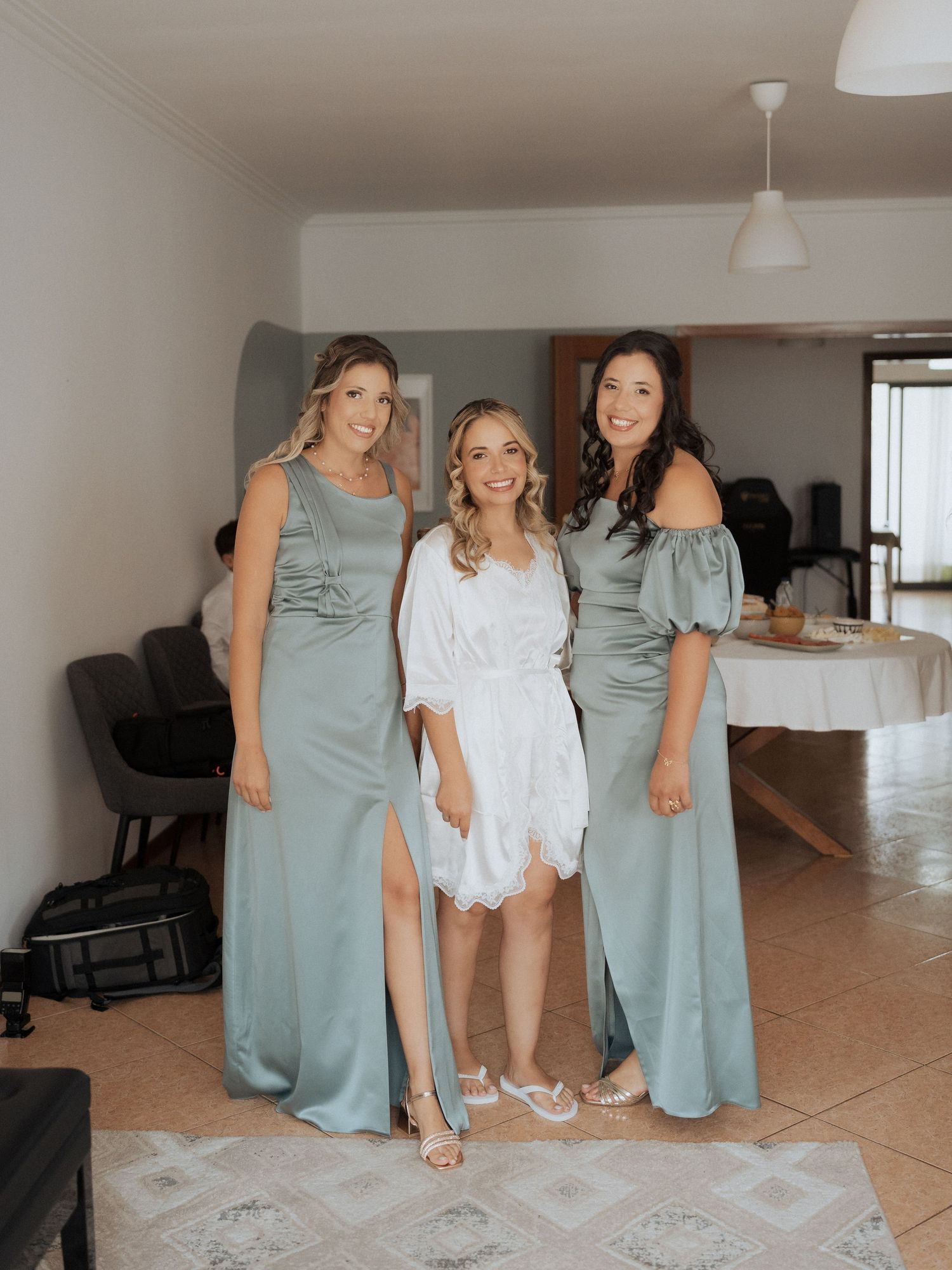 As damas de honra, vestidas com vestidos verde-sálvia, ajudam a noiva a calçar os sapatos durante os preparativos para o casamento.