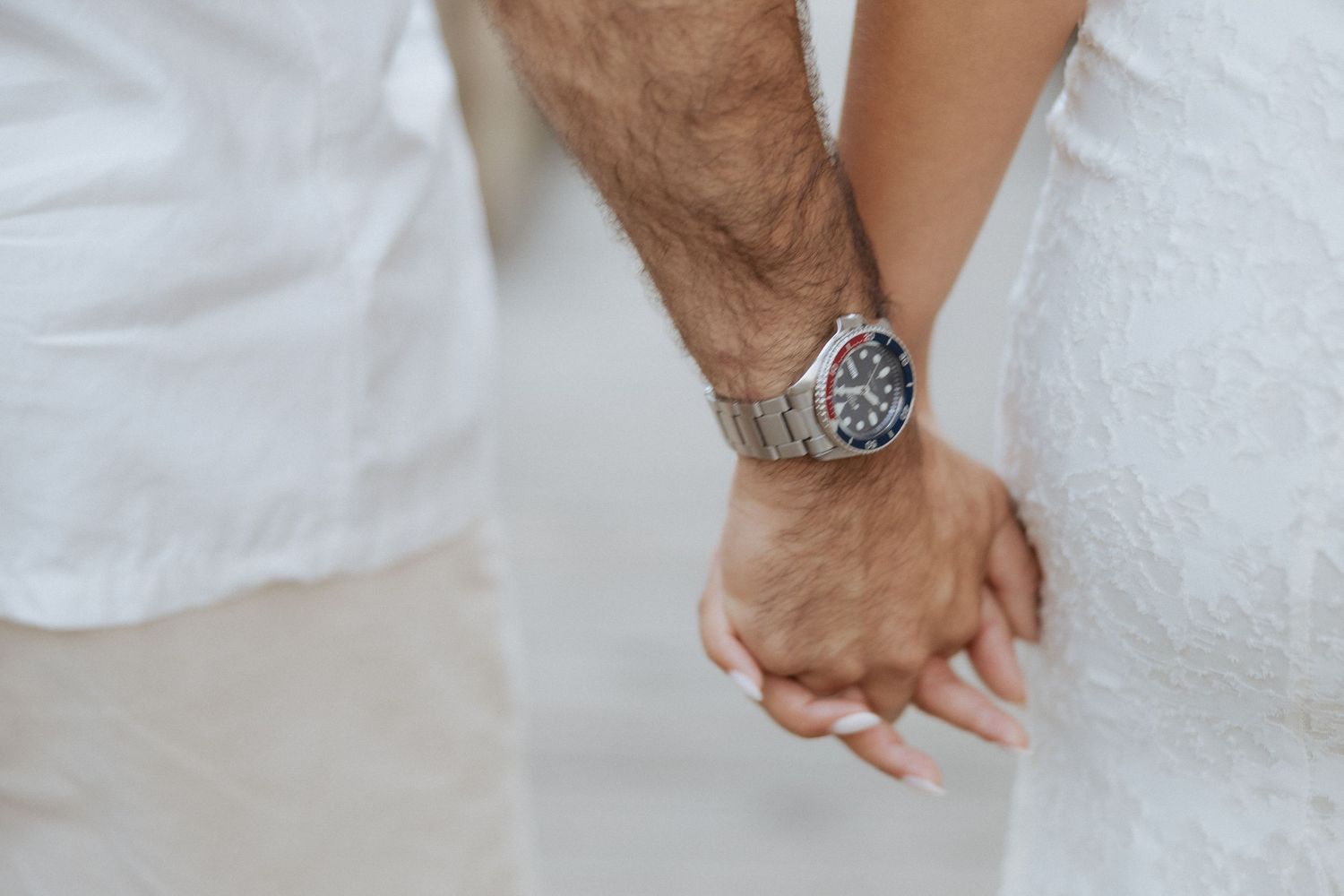 Close-up de um casal de mãos dadas, sendo que um deles usa um relógio prateado. Sessão de namoro na praia em Esposende