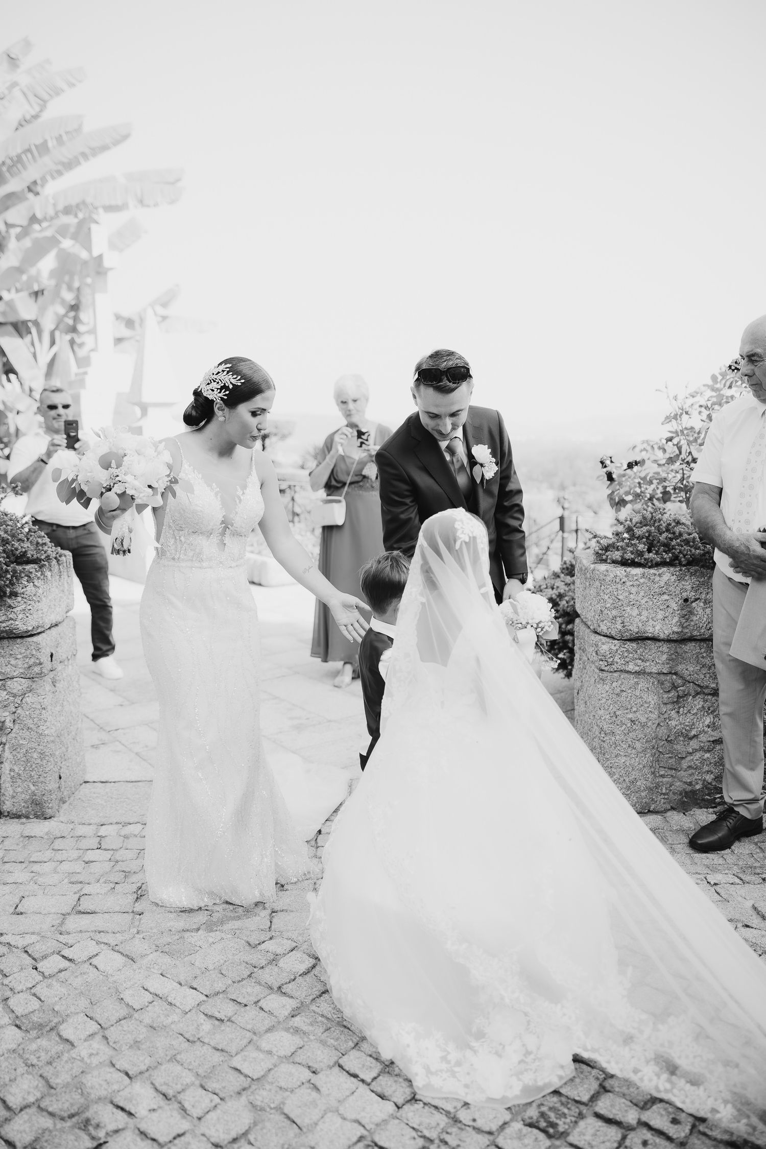 A joyful wedding celebration captured in black and white as guests toss confetti over the newlyweds on cobblestone streets.