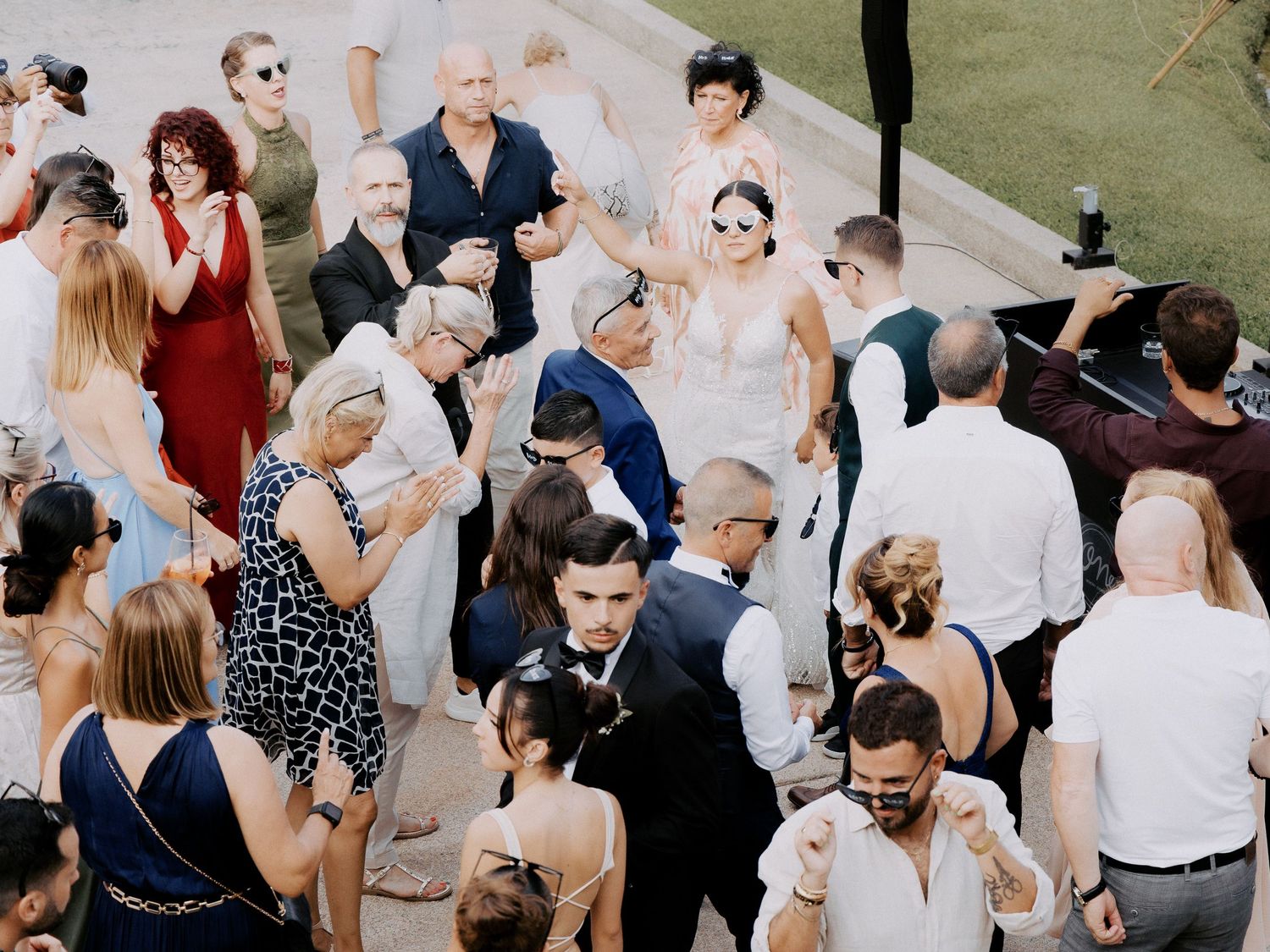 Wedding guests dance and celebrate on an outdoor dance floor during a daytime reception.