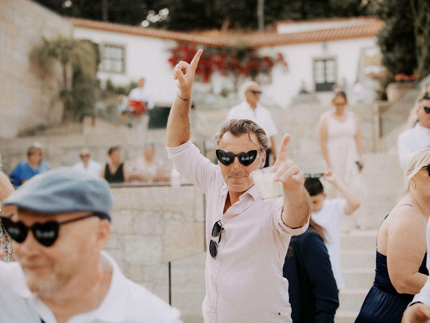 Wedding guests in white attire dance and celebrate at an outdoor reception with joyful expressions.