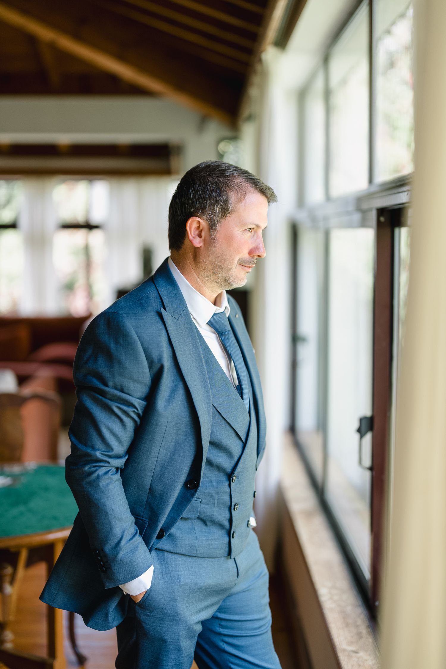 A person in a navy blue suit stands by a window in a series of connected photos showing different poses.