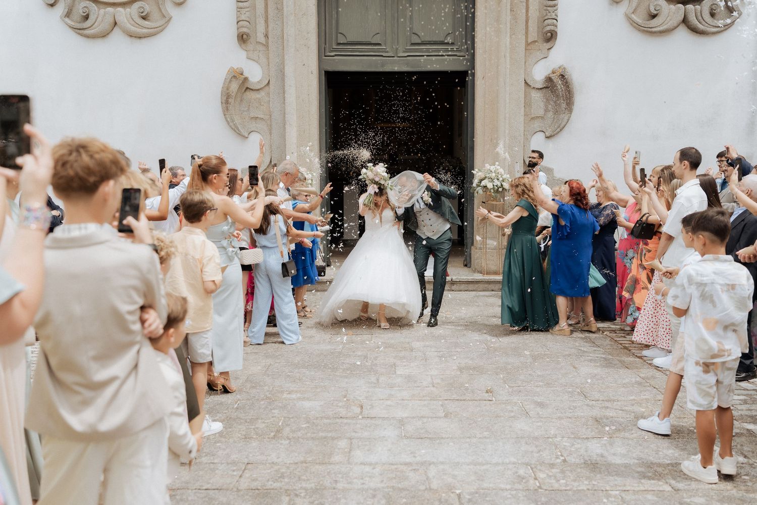 Os convidados do casamento jogam confete e comemoram do lado de fora de uma igreja histórica de pedra durante uma alegre saída da cerimônia.