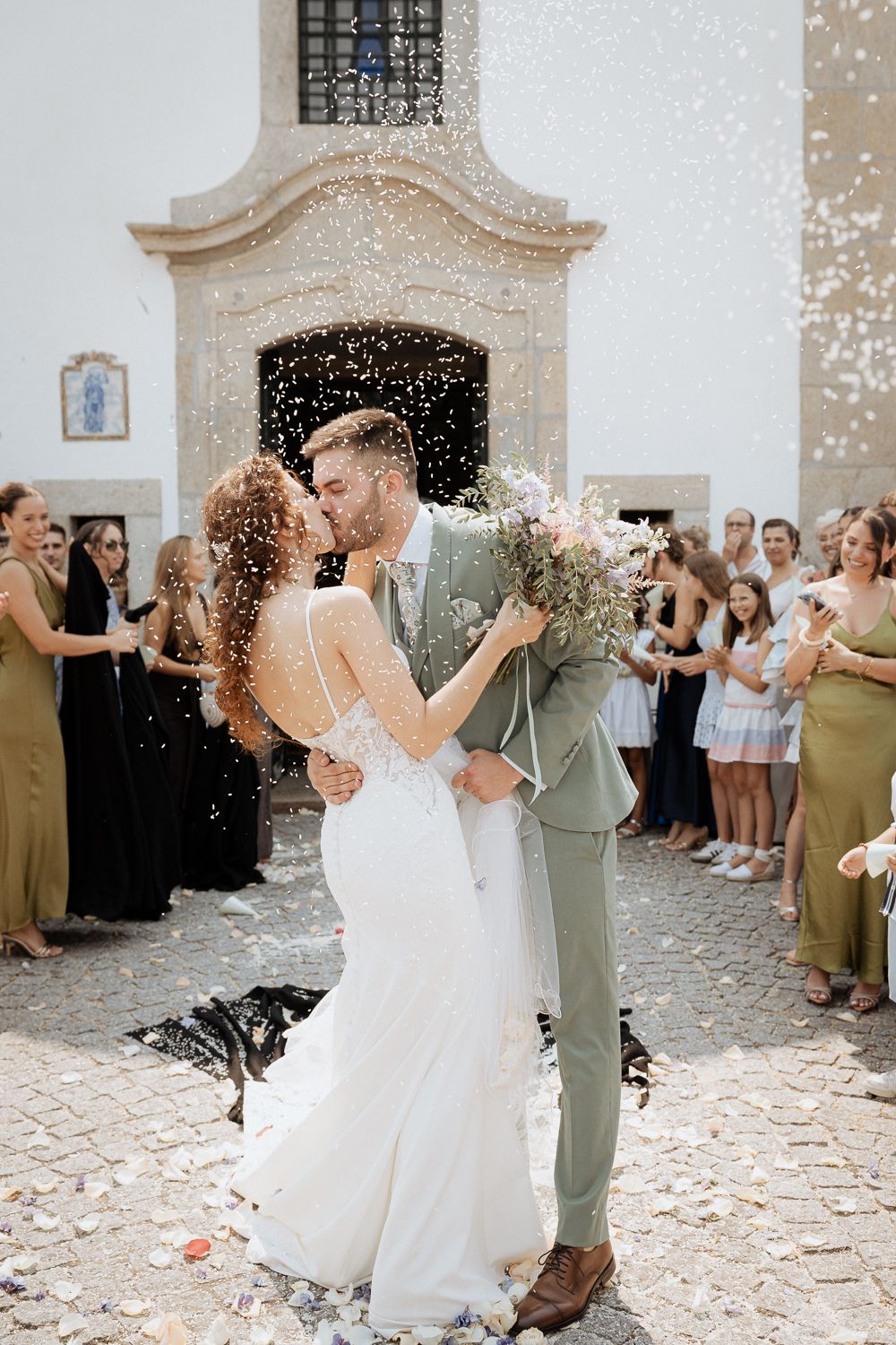 Newlyweds share their first dance surrounded by guests throwing confetti in a beautiful stone courtyard.