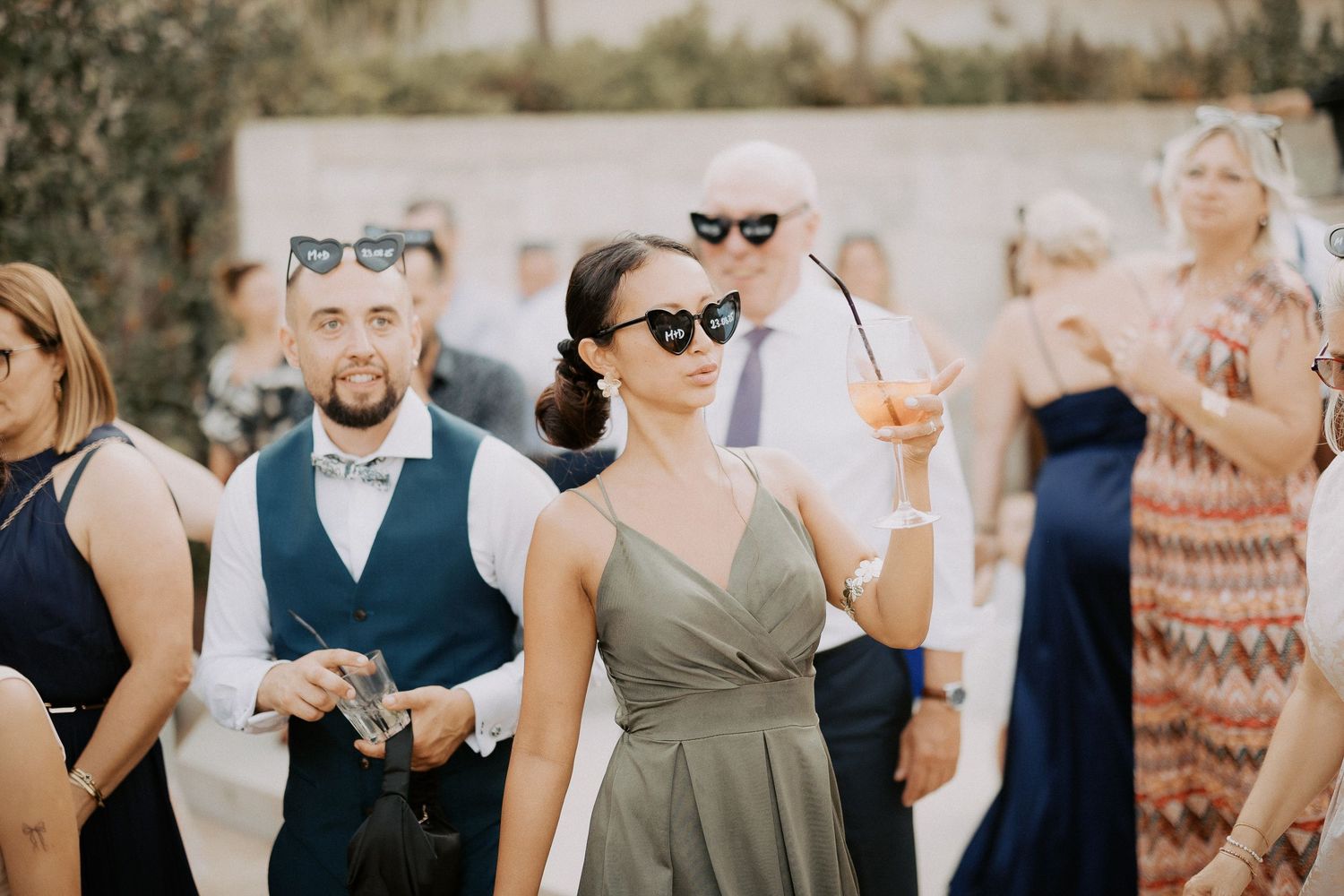 A collage of wedding party photos showing people in formal attire celebrating outdoors with sunglasses and drinks.