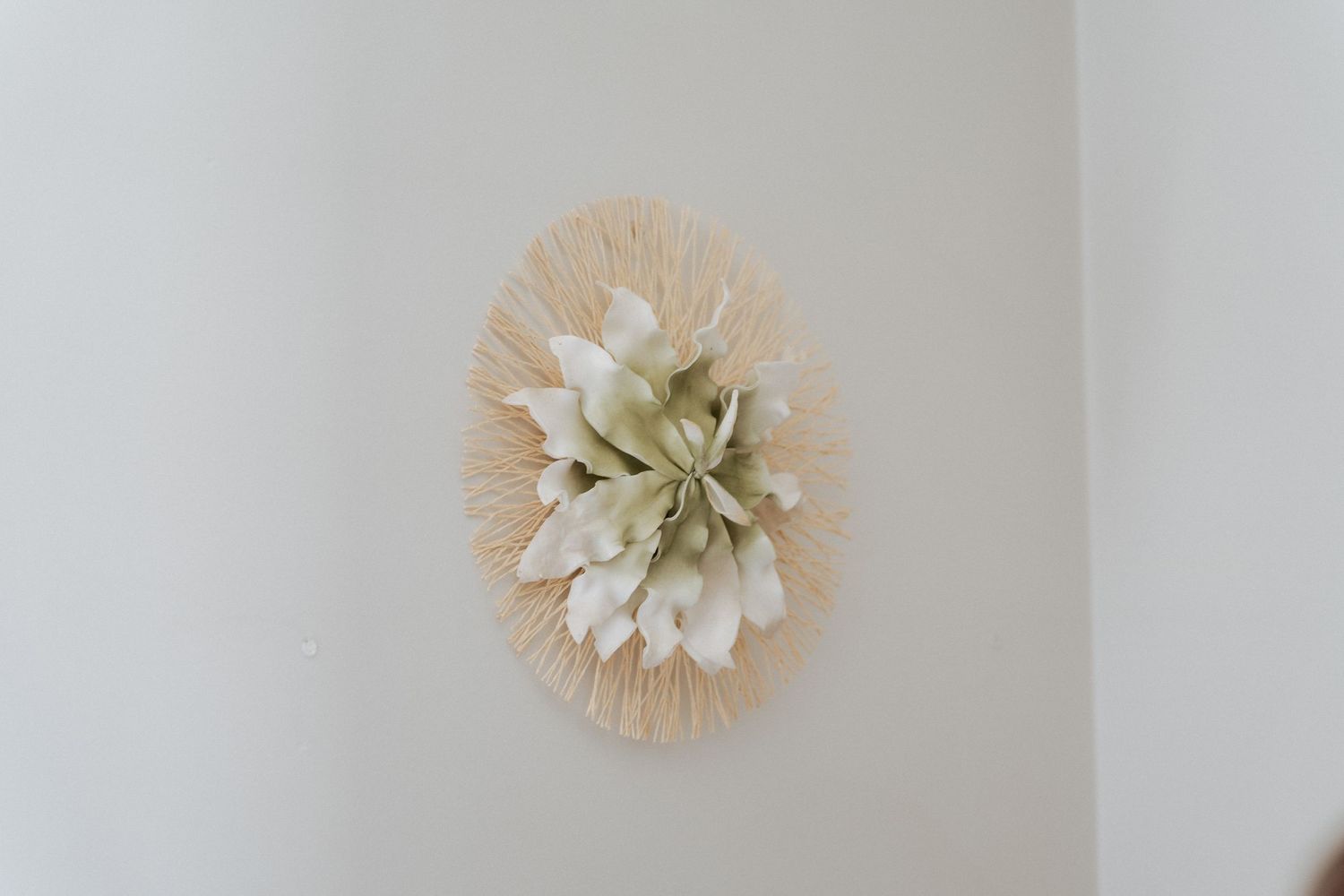 Instalação decorativa de flores de papel em tons neutros sobre uma parede branca.