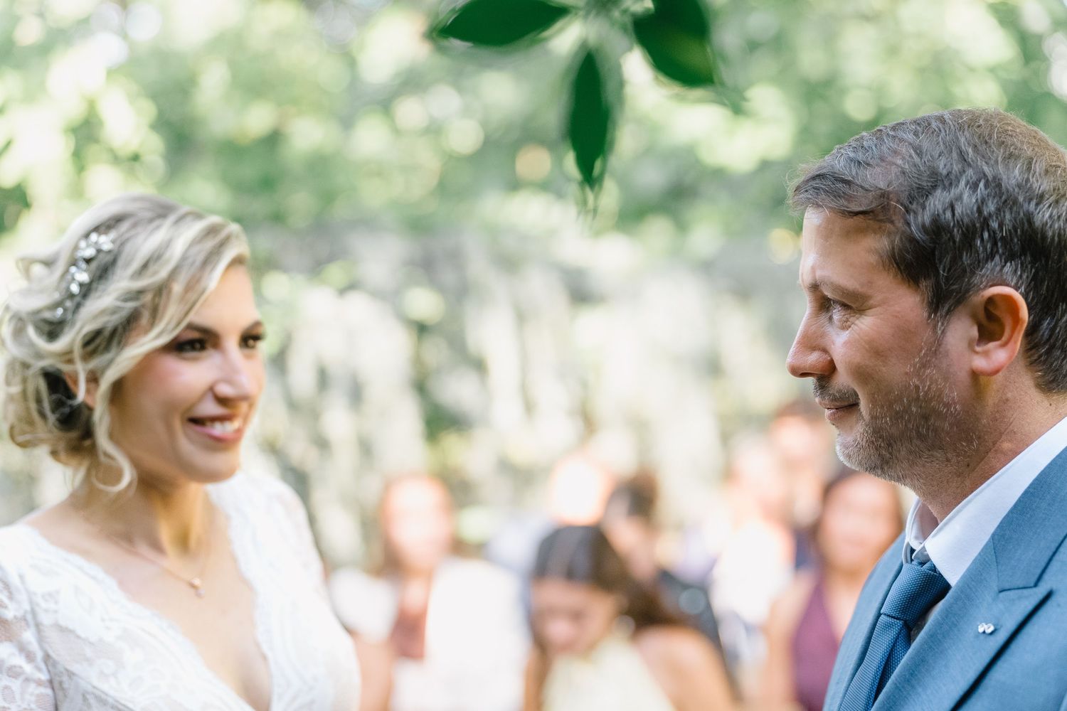 A couple shares a joyful moment together during an outdoor celebration surrounded by guests and greenery.