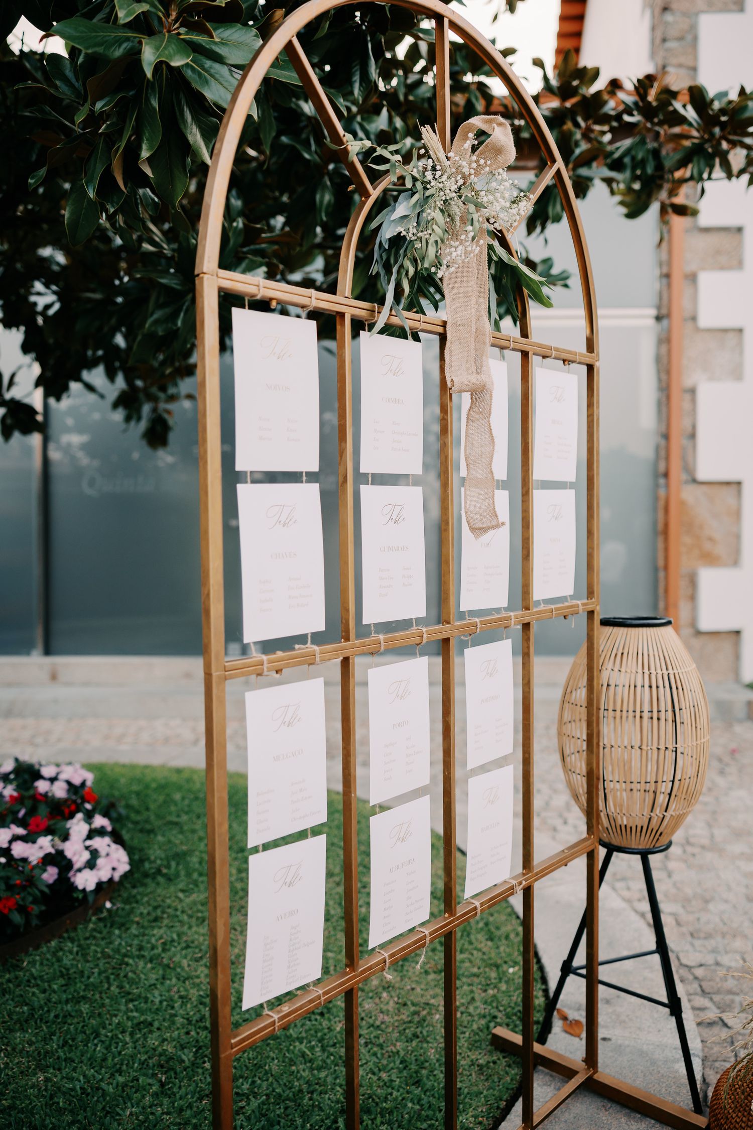 Elegant arched wooden seating chart display with white cards and a decorative lantern at an outdoor wedding venue.