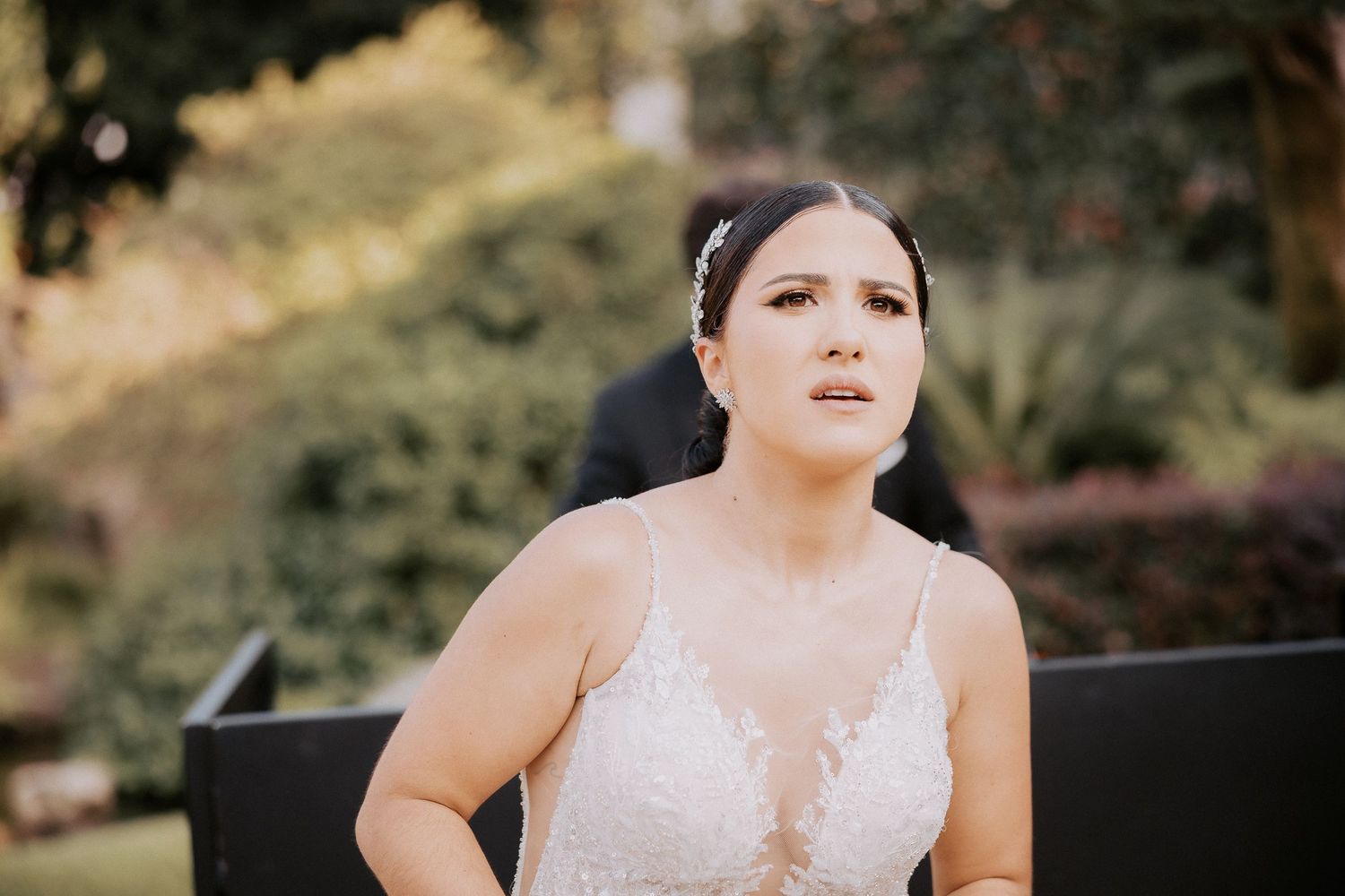 A bride in a lace wedding dress sits outdoors during a golden hour photoshoot.