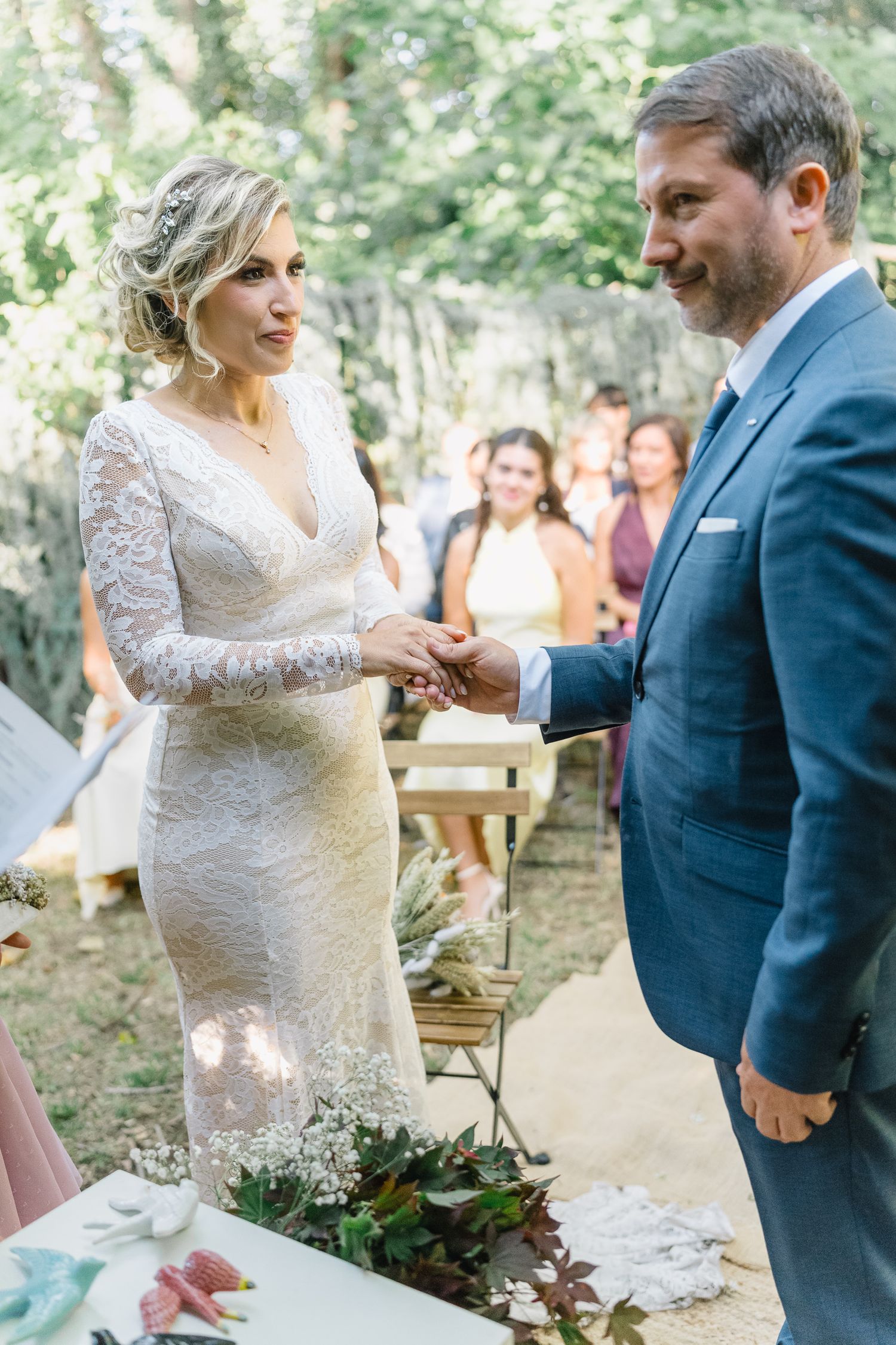 A couple exchanges rings during an intimate outdoor forest wedding ceremony with guests seated in the background.