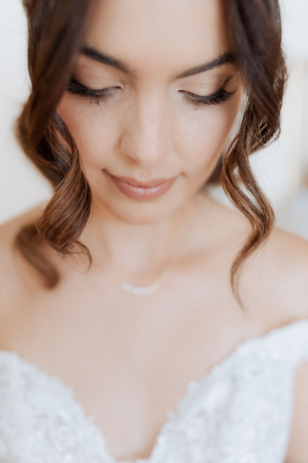 Close up portrait with soft makeup and wavy brown hair wearing a white lace wedding dress.