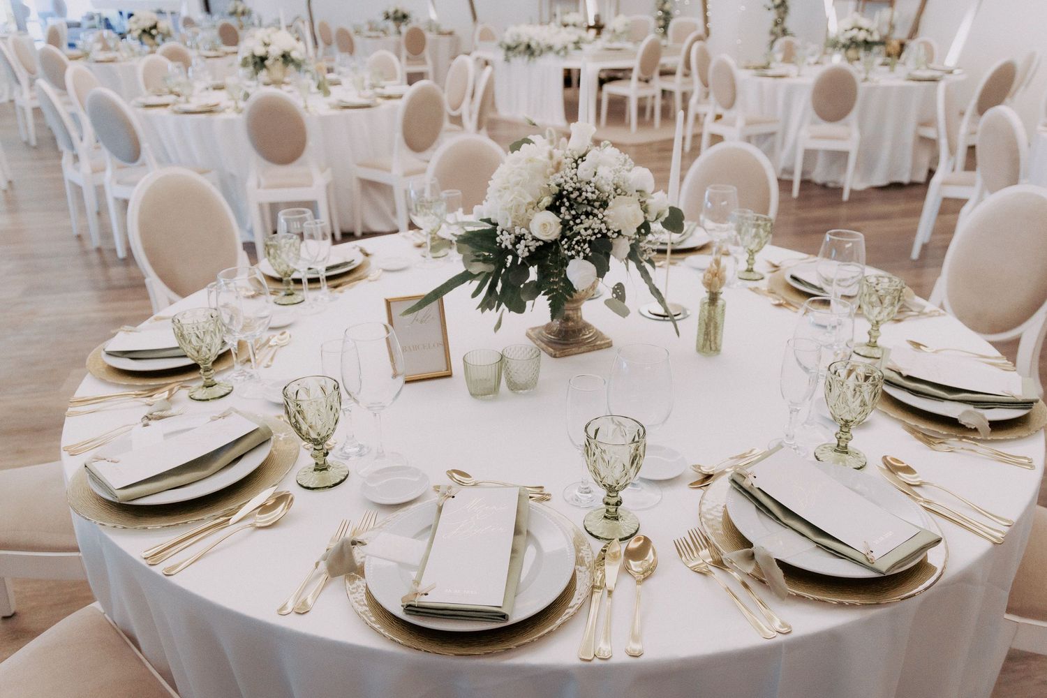 Elegant round tables with white linens, gold chargers, and floral centerpieces set for a formal wedding reception.