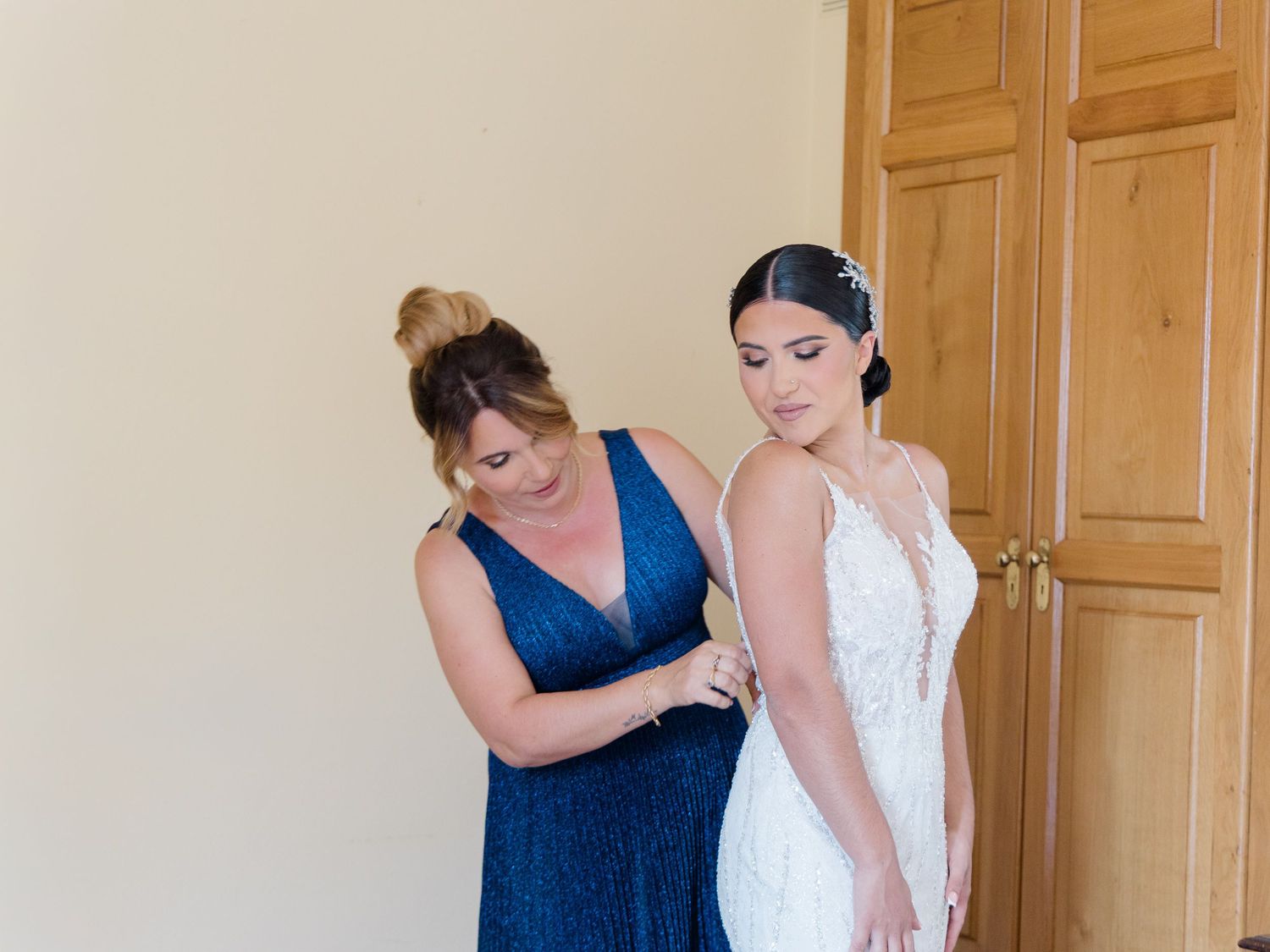 A person in a navy blue dress helps adjust a white wedding gown on someone during a formal preparation moment.