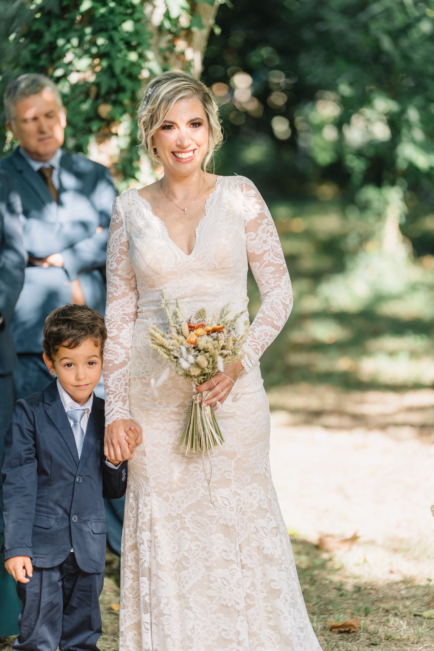 A sweet outdoor wedding moment captured in a garden setting with a lace dress and navy suit.