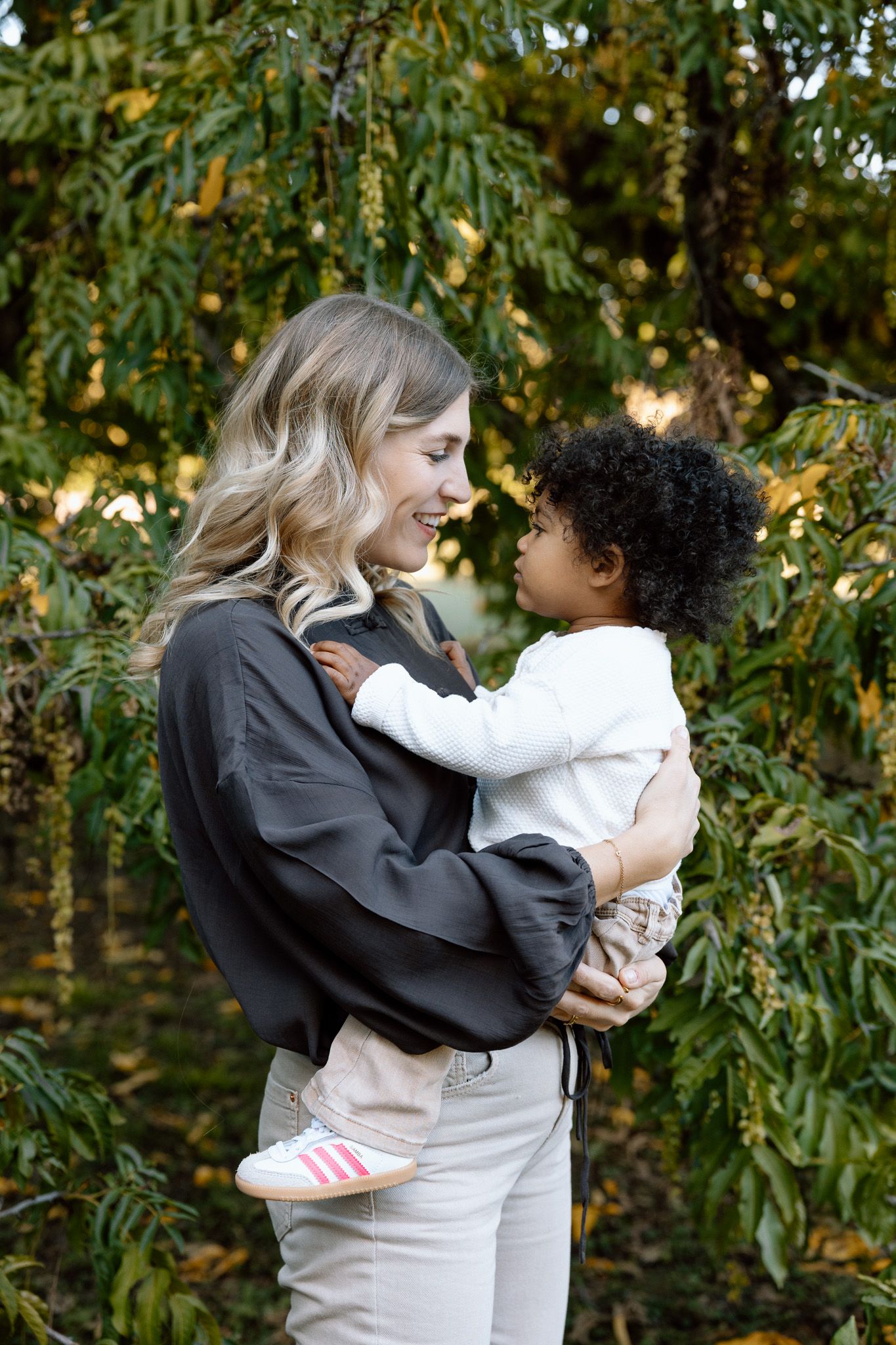 Mother and toddler looking at each other between green leaves, Familienshooting