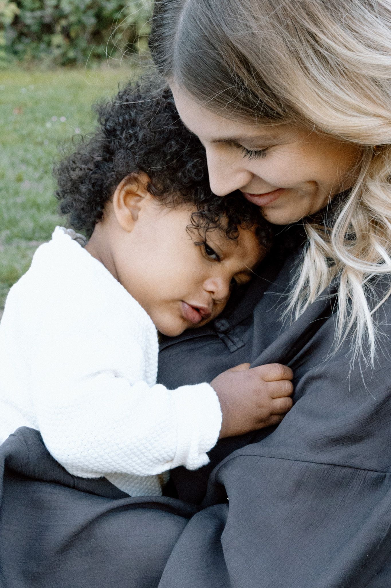 Close-up of a mother holding her toddler close in the grass, Familienfotografie