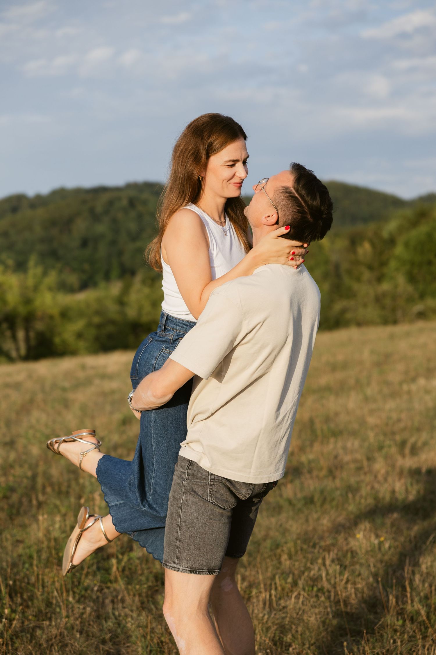 Man lifting his partner off the ground in a meadow, hills in the background, Paarfotografie Stuttgart