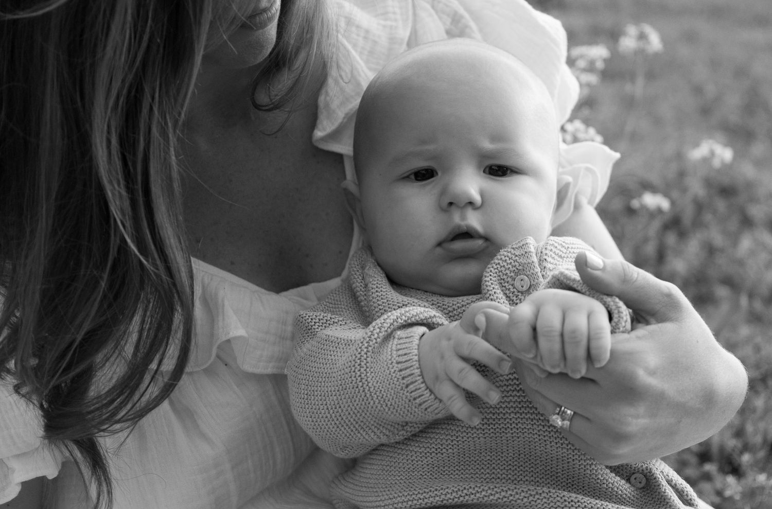 Black and white close-up of mother cradling infant in knit sweater outdoors.