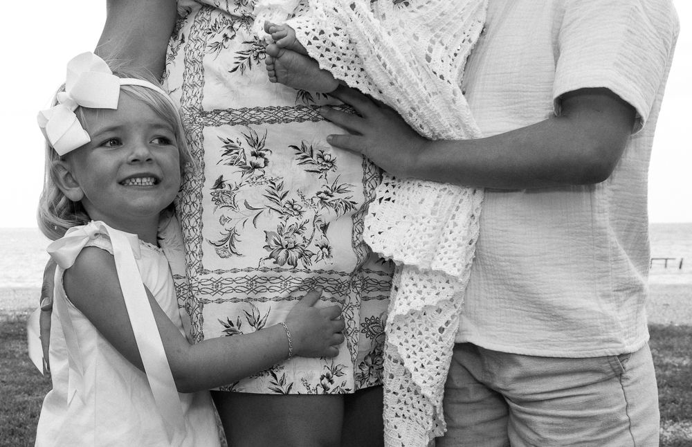 Young girl hugging pregnant mother's belly during outdoor maternity photo session.