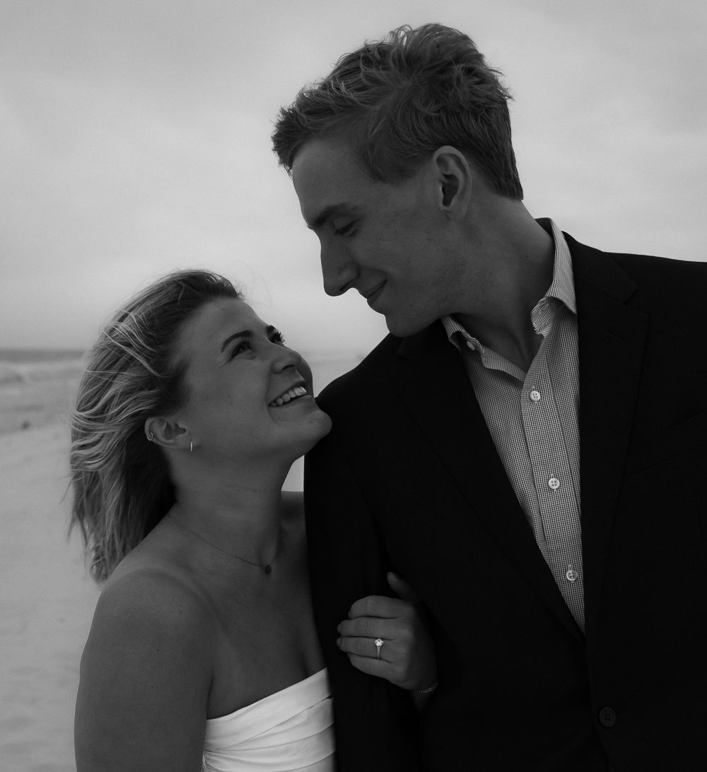 Happy couple smiles at each other on the beach in a romantic black and white portrait photo.
