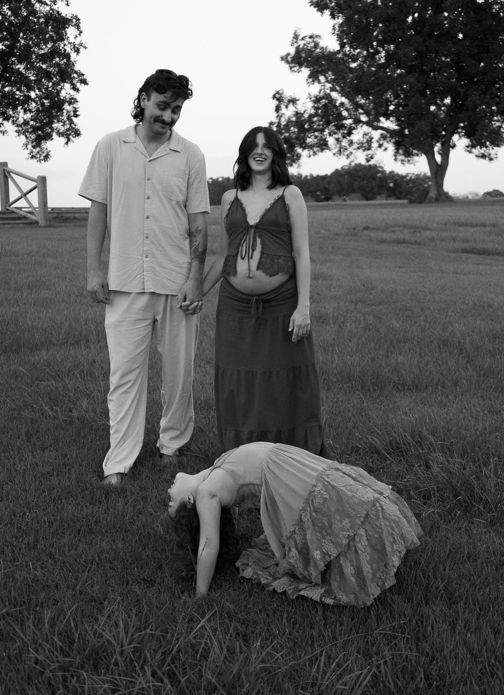 Black and white photo of a couple holding hands in a field, with a child bending down in front of them.