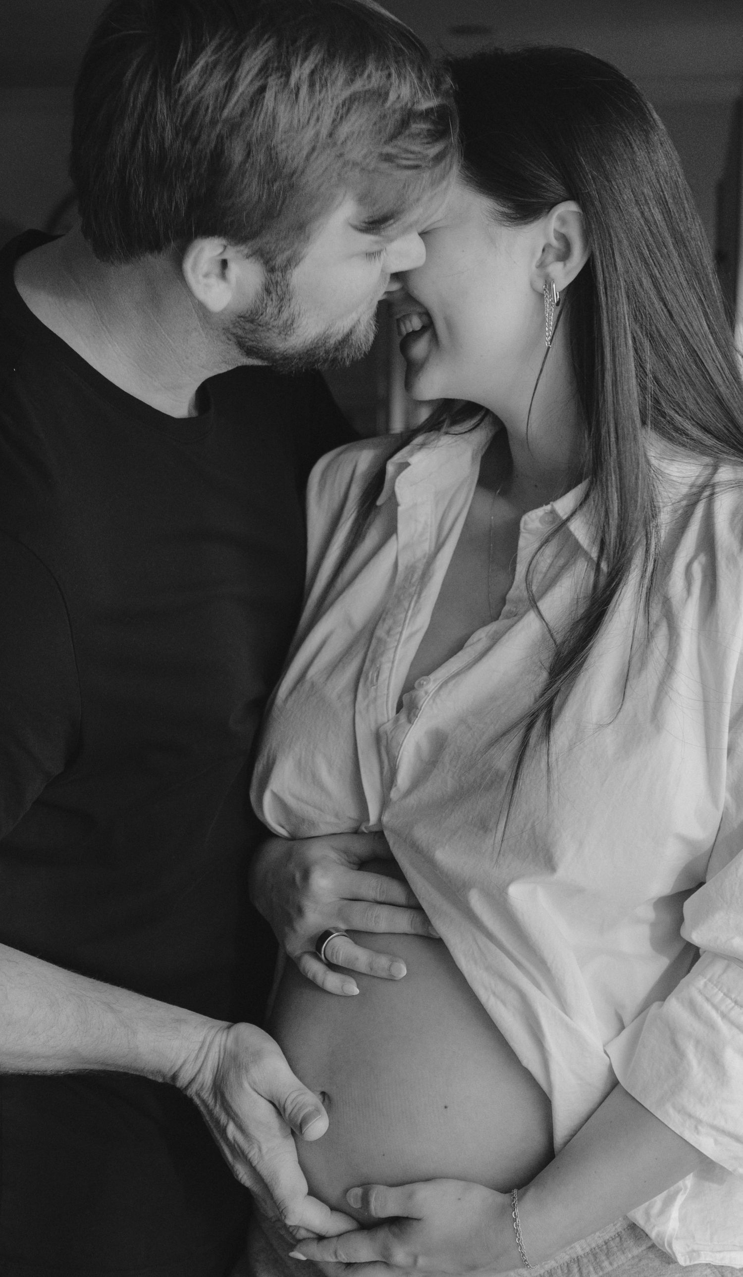 Black and white photo of a couple sharing a tender moment, hands cradling a pregnant belly.