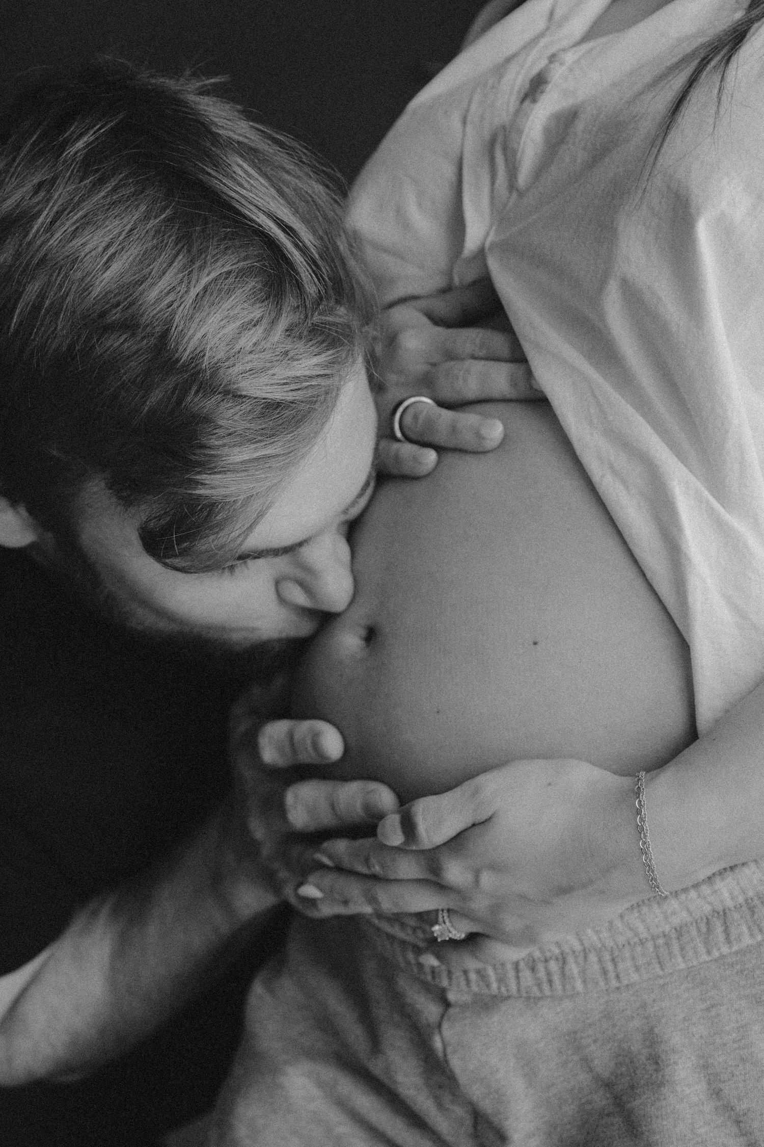 Black and white close-up of a man gently kissing a pregnant woman's bare baby bump.