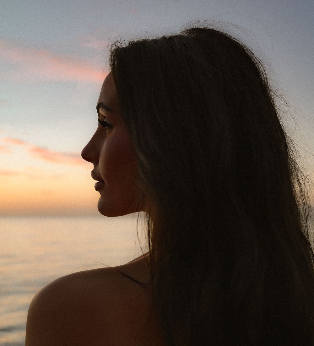 Stunning profile silhouette of brunette woman with long hair against colorful ocean sunset sky.