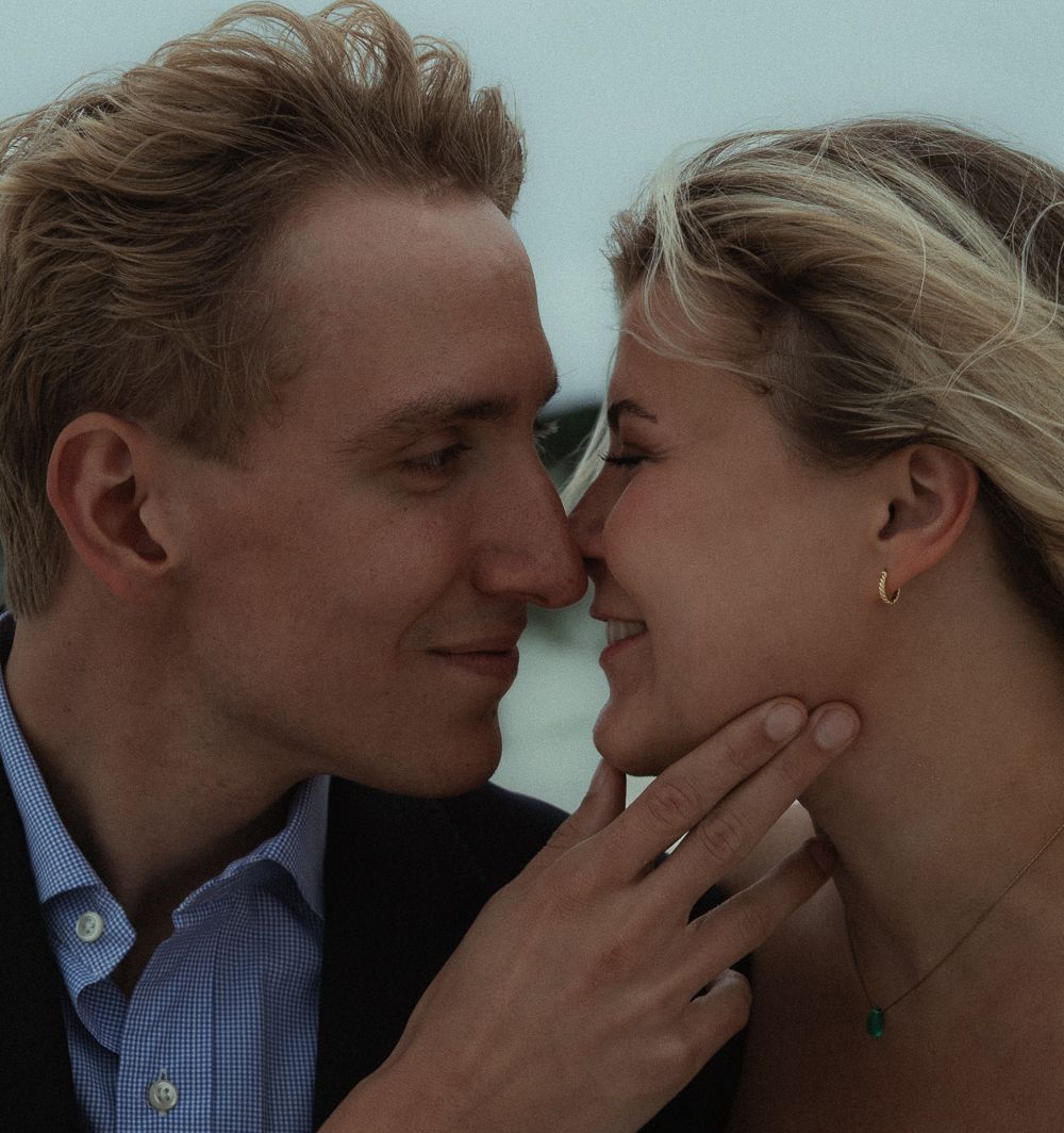 Couple shares an intimate romantic moment, woman displaying engagement ring while man cups her face.