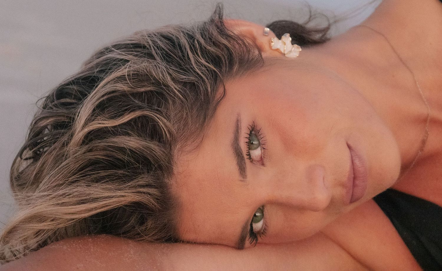 Close-up portrait of woman with highlighted hair and green eyes lying on beach.