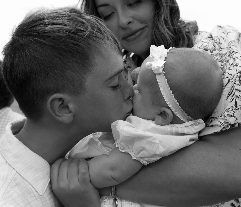 Tender black and white photo of parents kissing their newborn baby girl in floral headband.