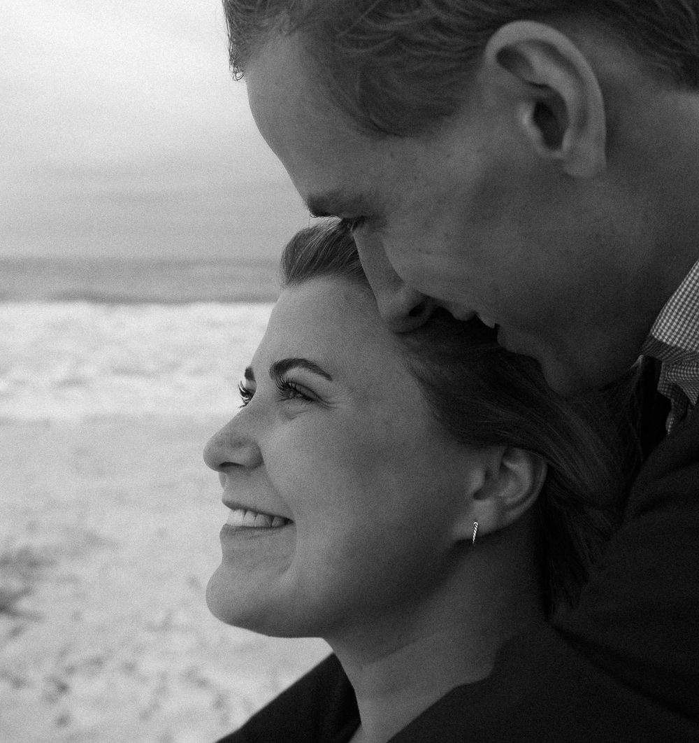 Black and white romantic beach portrait of smiling couple, man kissing womans forehead.
