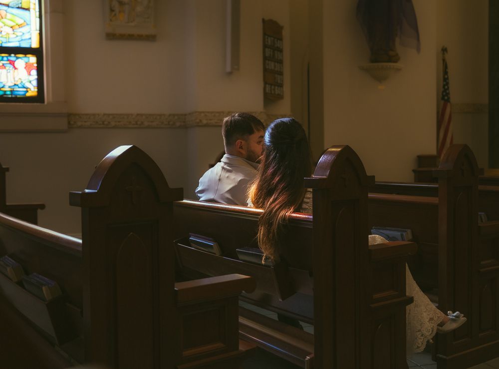 Romantic couple sharing an intimate moment in a dimly lit church pew with stained glass windows.