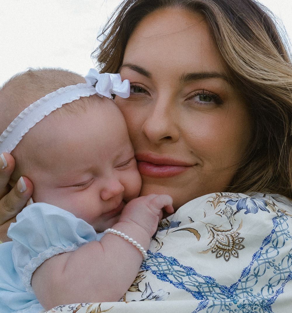 Smiling mother snuggling sleeping newborn baby in soft outdoor light.