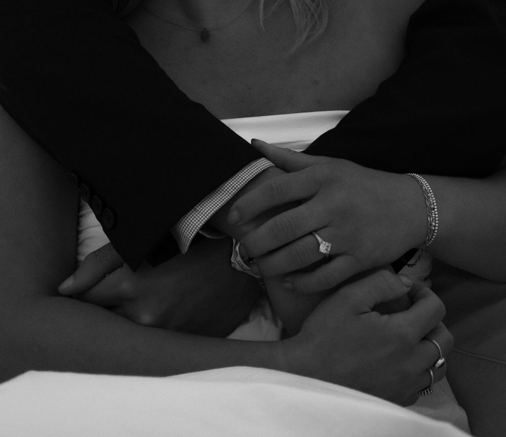 Close-up black and white photo of couple holding hands showing engagement ring and bracelet.