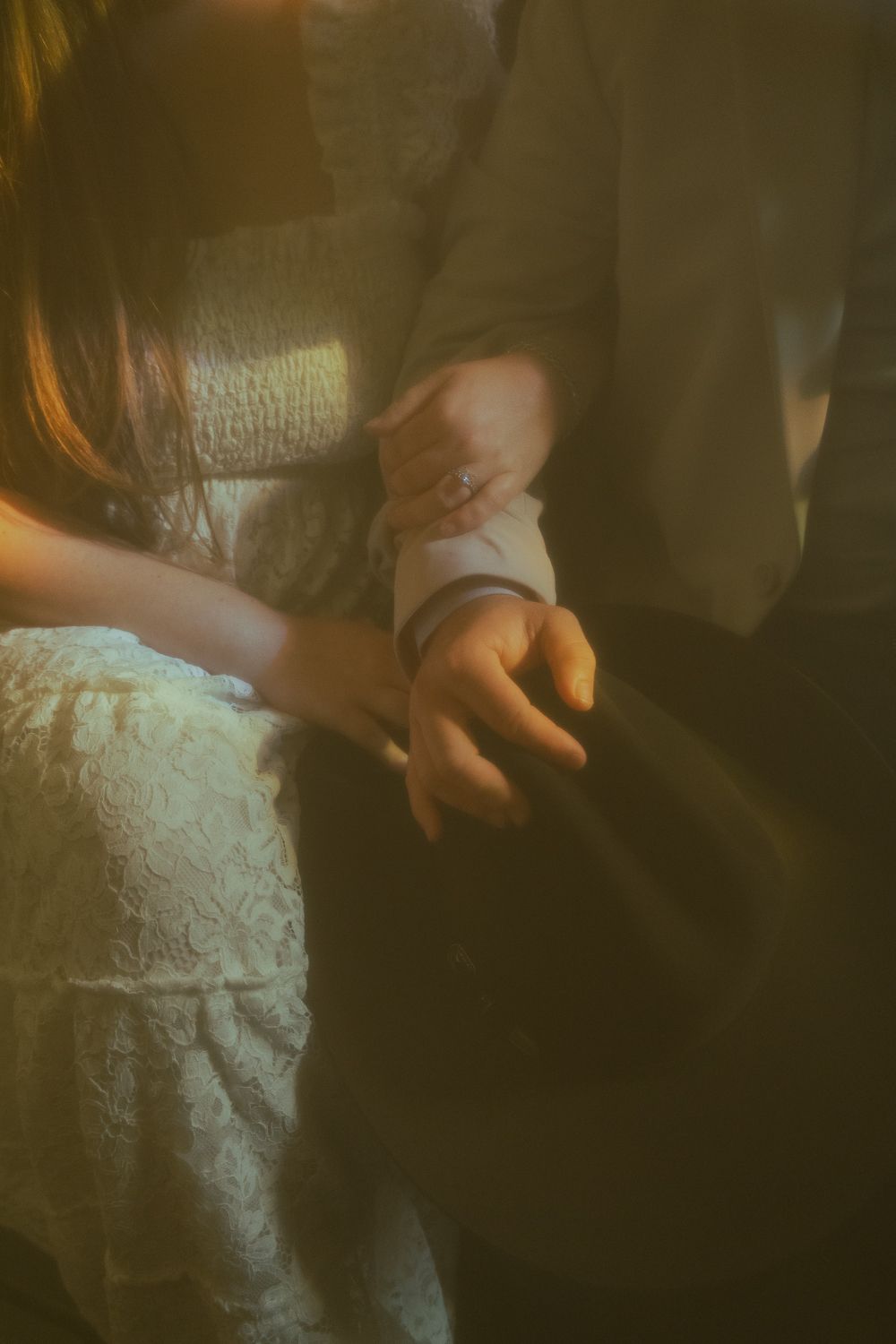 Close-up of a bride and groom holding hands, wearing wedding attire, bathed in warm golden light.