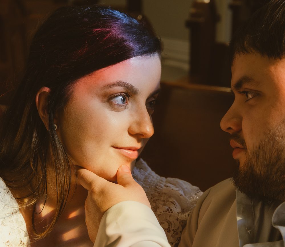 Close-up of a bride with blue eyes gazing at her groom in warm romantic lighting.