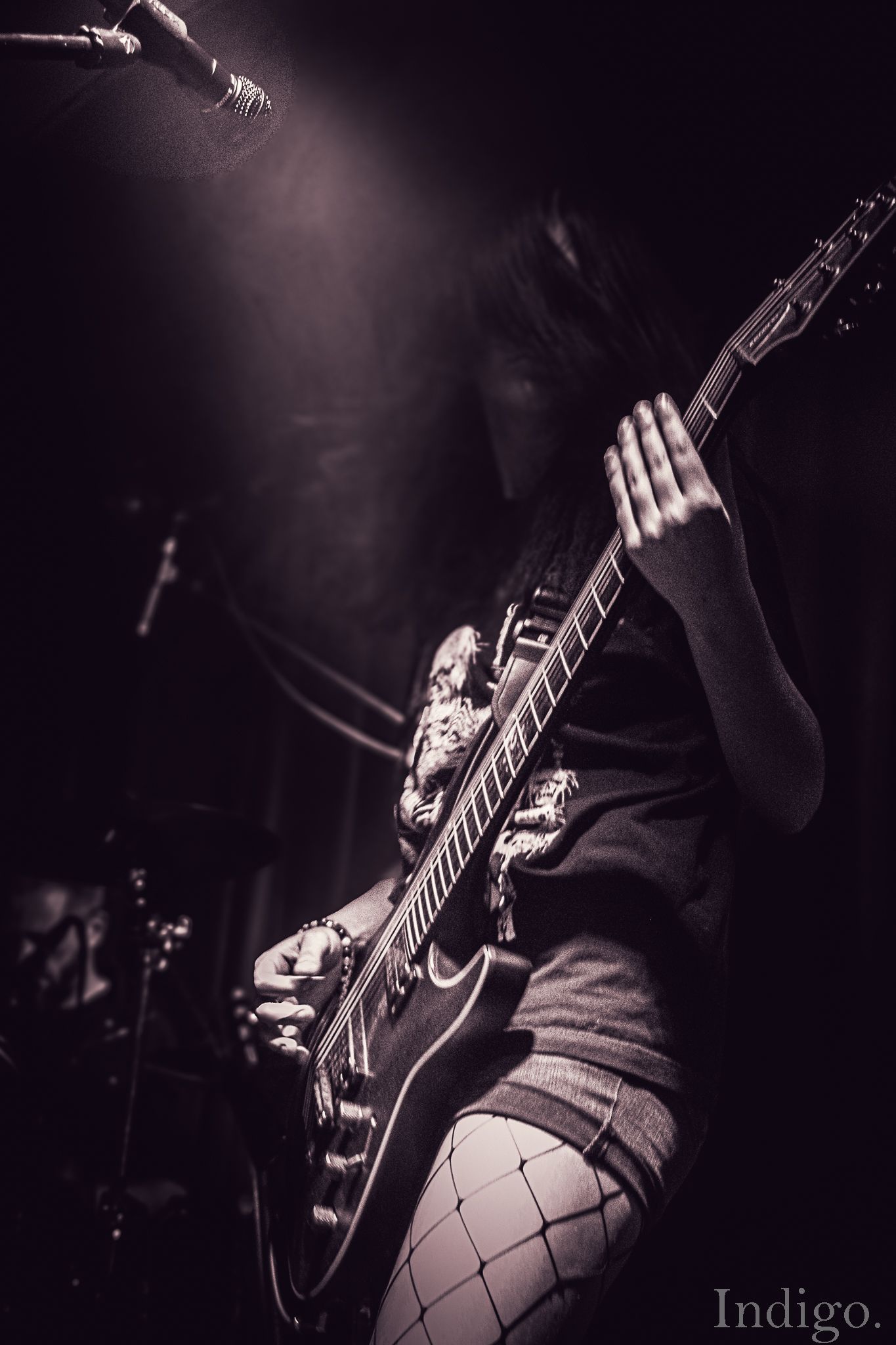 Dark concert photography showing a guitarist performing on stage.