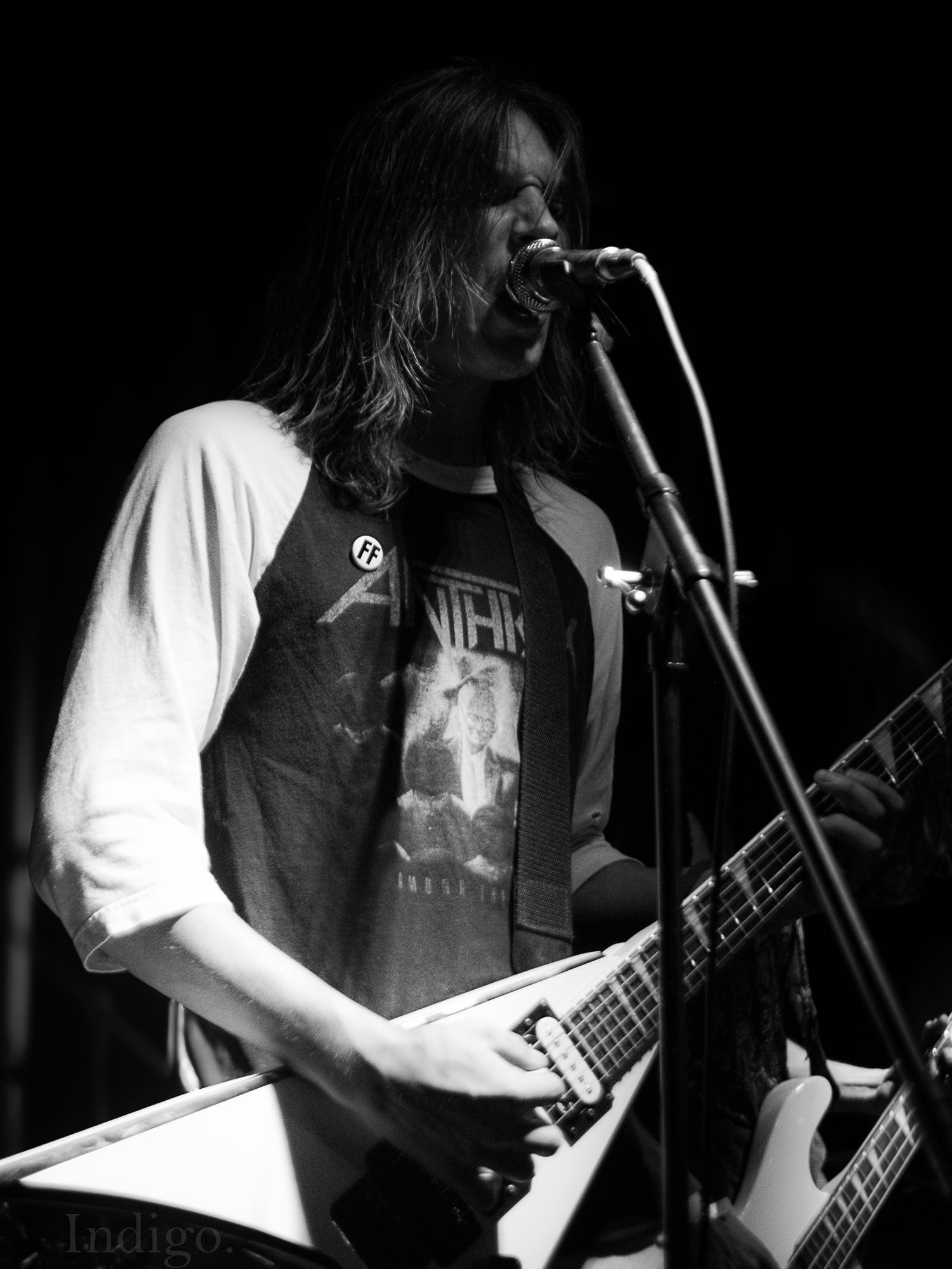 Black and white photo of musician playing guitar on dimly lit concert stage.