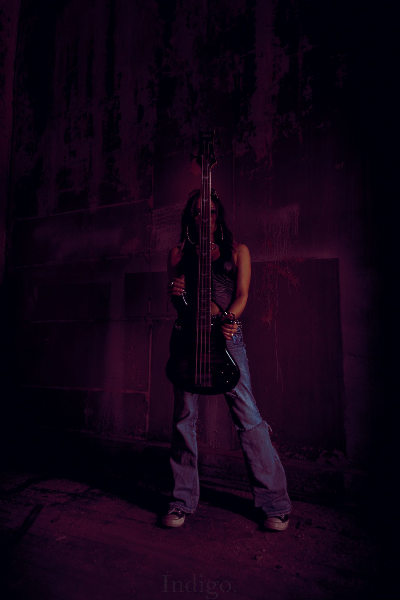 Silhouette of bass guitar player against dark purple stage lighting.