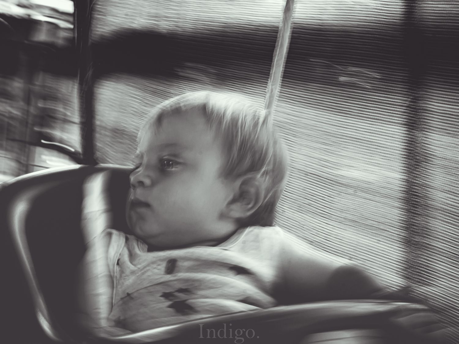 A young child sleeps peacefully in a car seat while traveling, captured in black and white photography.
