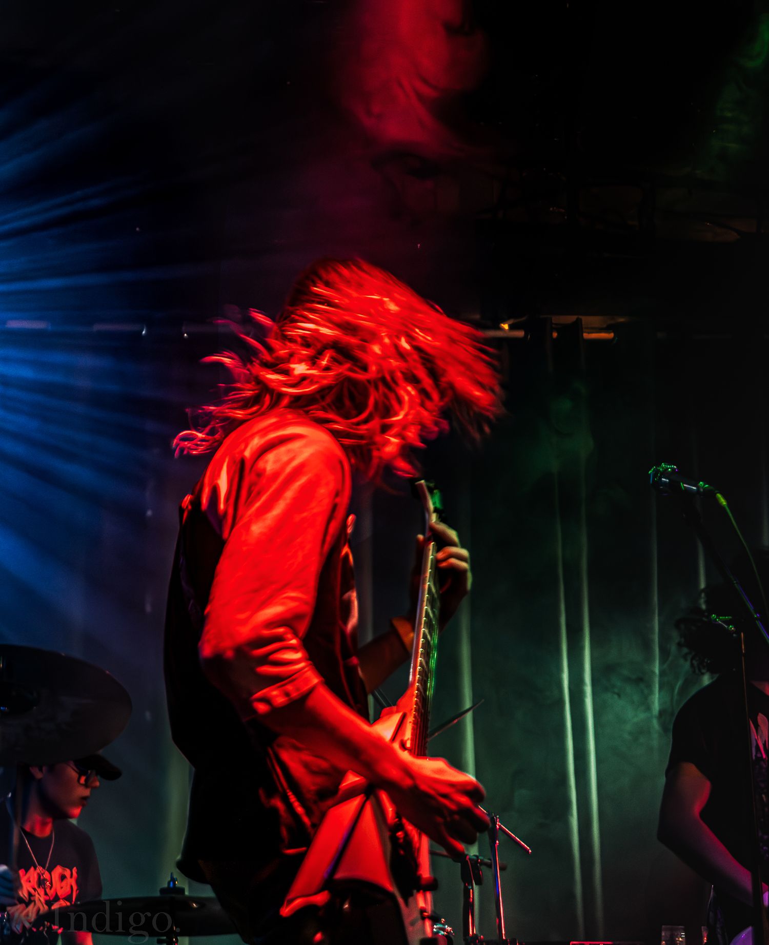Dynamic concert shots with dramatic red lighting capture musicians headbanging during performance.