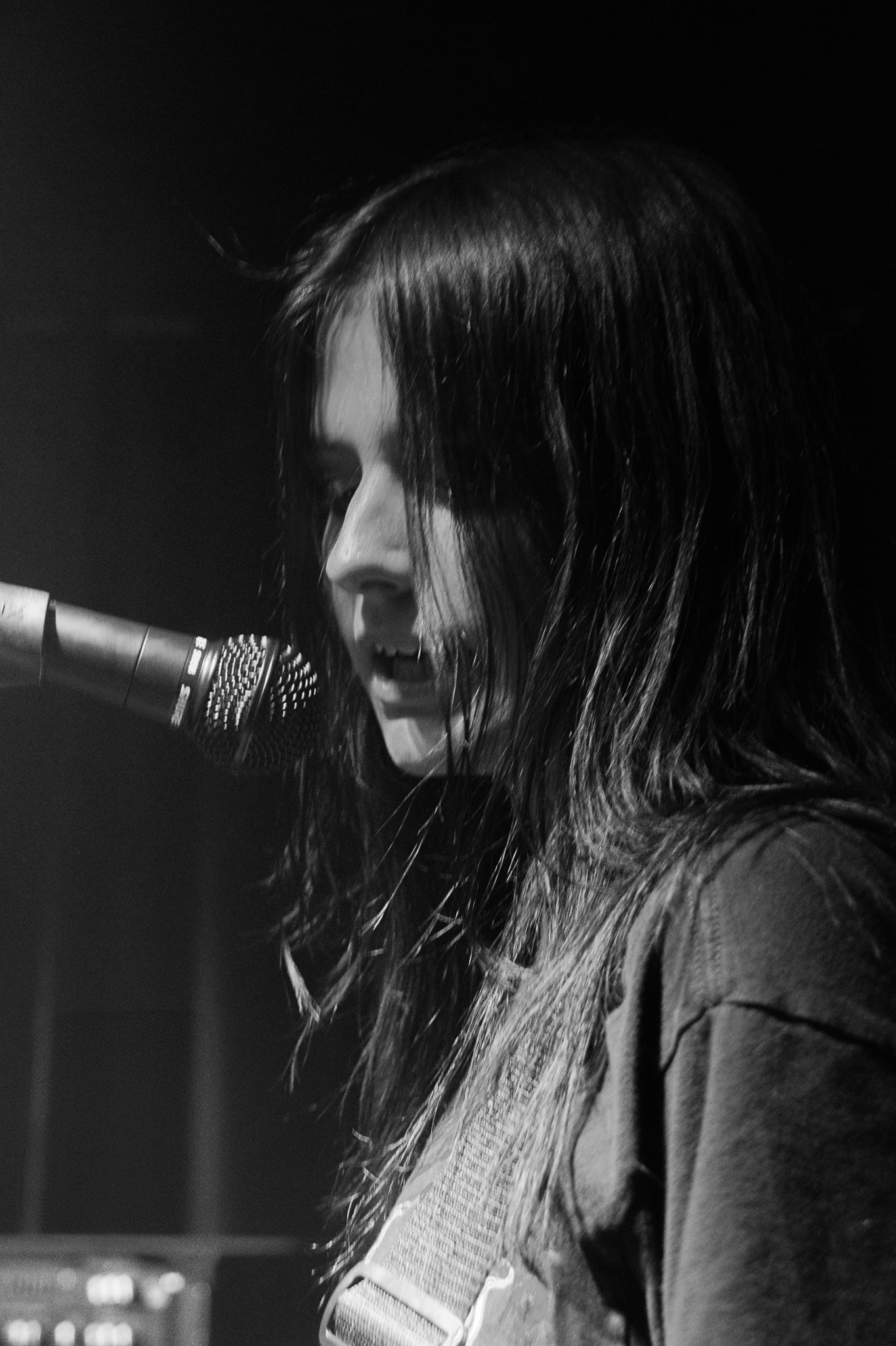 Black and white concert photo of performer at microphone with dramatic side lighting.