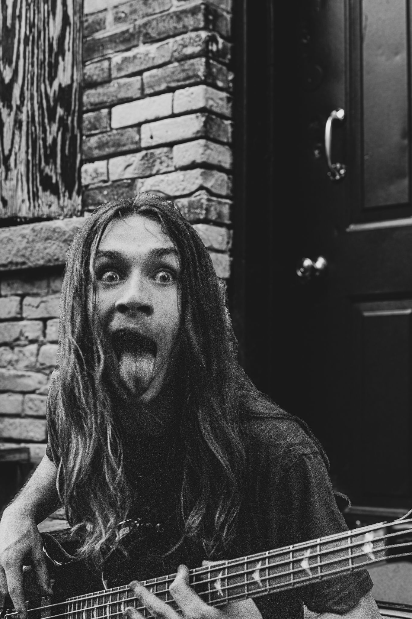 Energetic bassist making silly face while holding bass guitar against brick wall.
