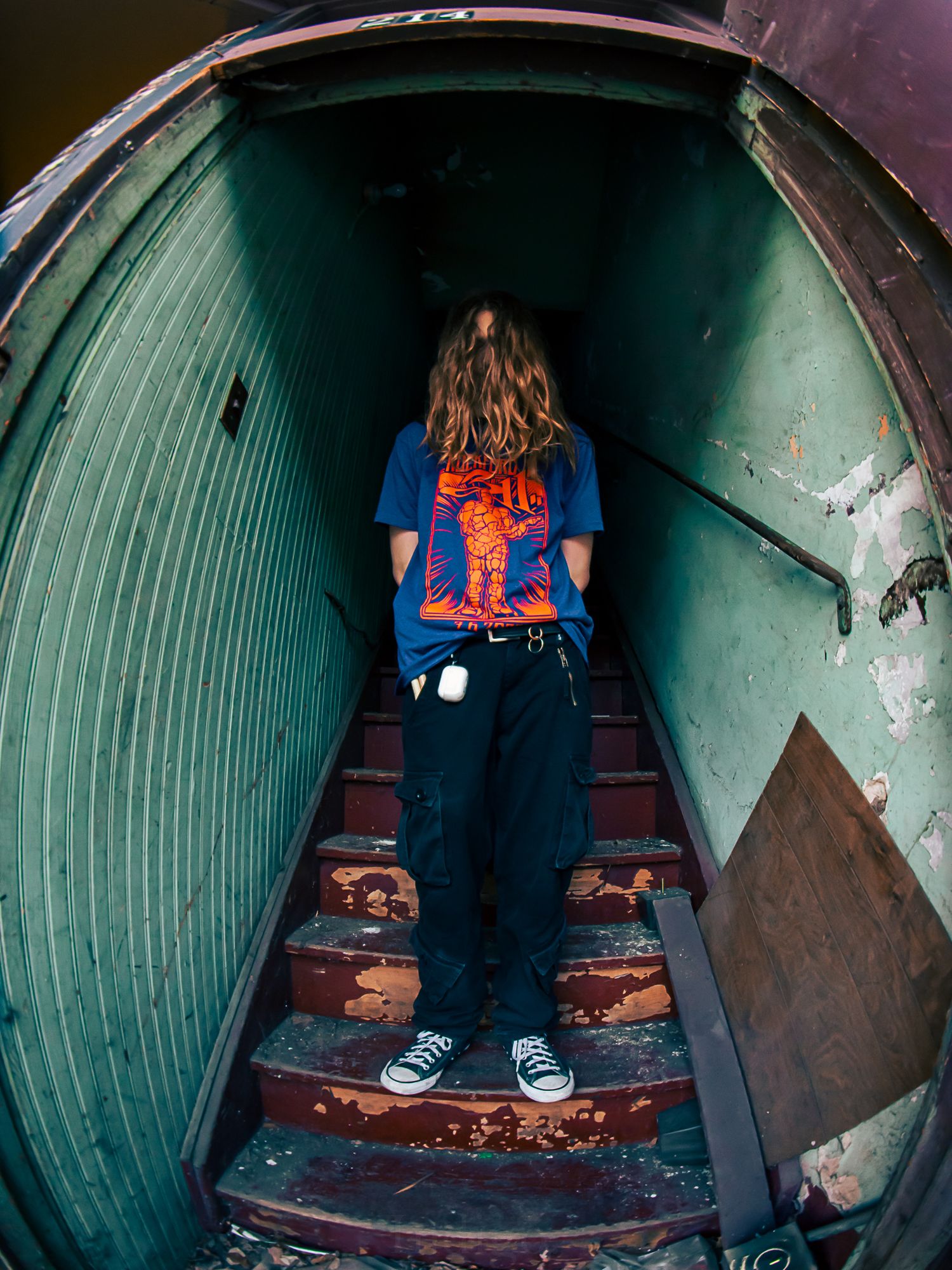 Person walking down dark green tunnel staircase wearing blue shirt and dark pants.